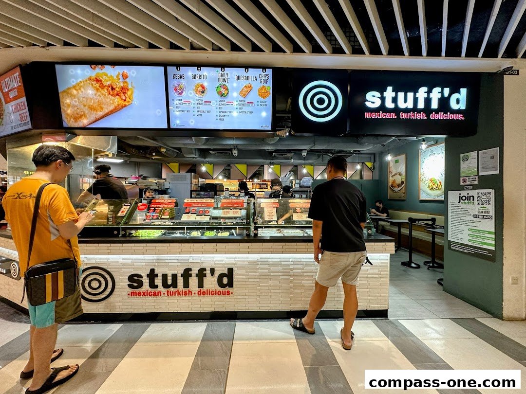 Customers ordering at a food counter with a menu board displaying various dishes.