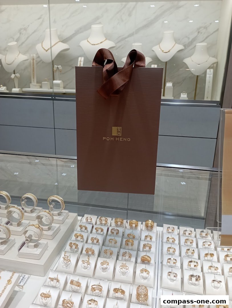 A brown shopping bag with the Poh Heng logo is displayed in front of a jewelry store display.