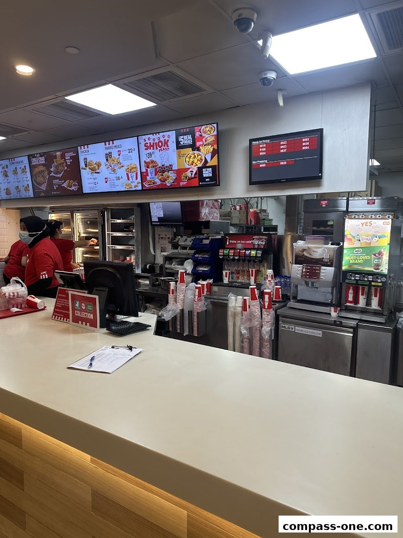 Interior view of a KFC restaurant counter with digital menus and staff serving customers.