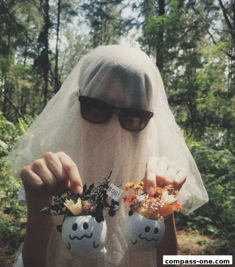 A person dressed as a ghost holds two small potted plants with spooky faces.