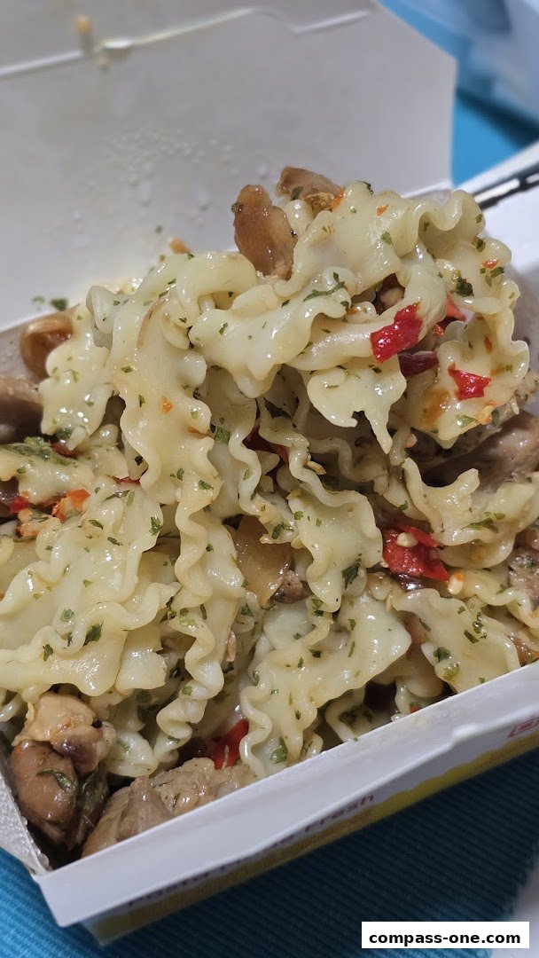 A close-up of freshly made pasta with chicken and chili in a takeaway container.