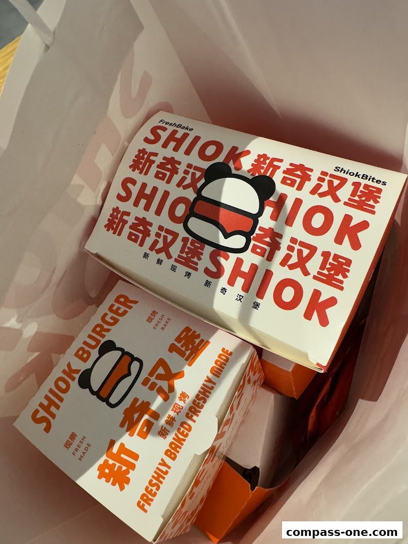 Two Shiok Burger takeaway boxes are shown inside a white paper bag.