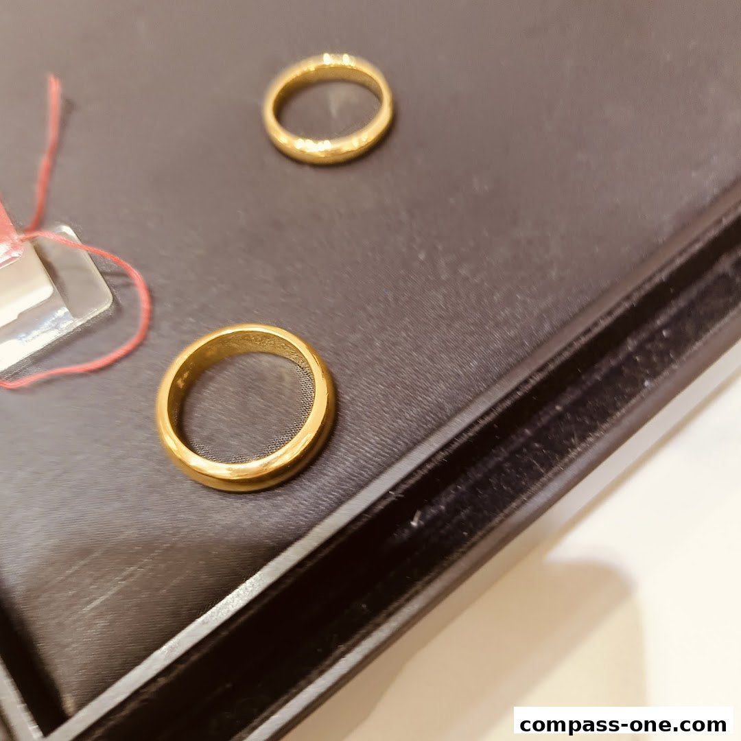 Two elegant gold rings displayed on a dark surface, one with a price tag.