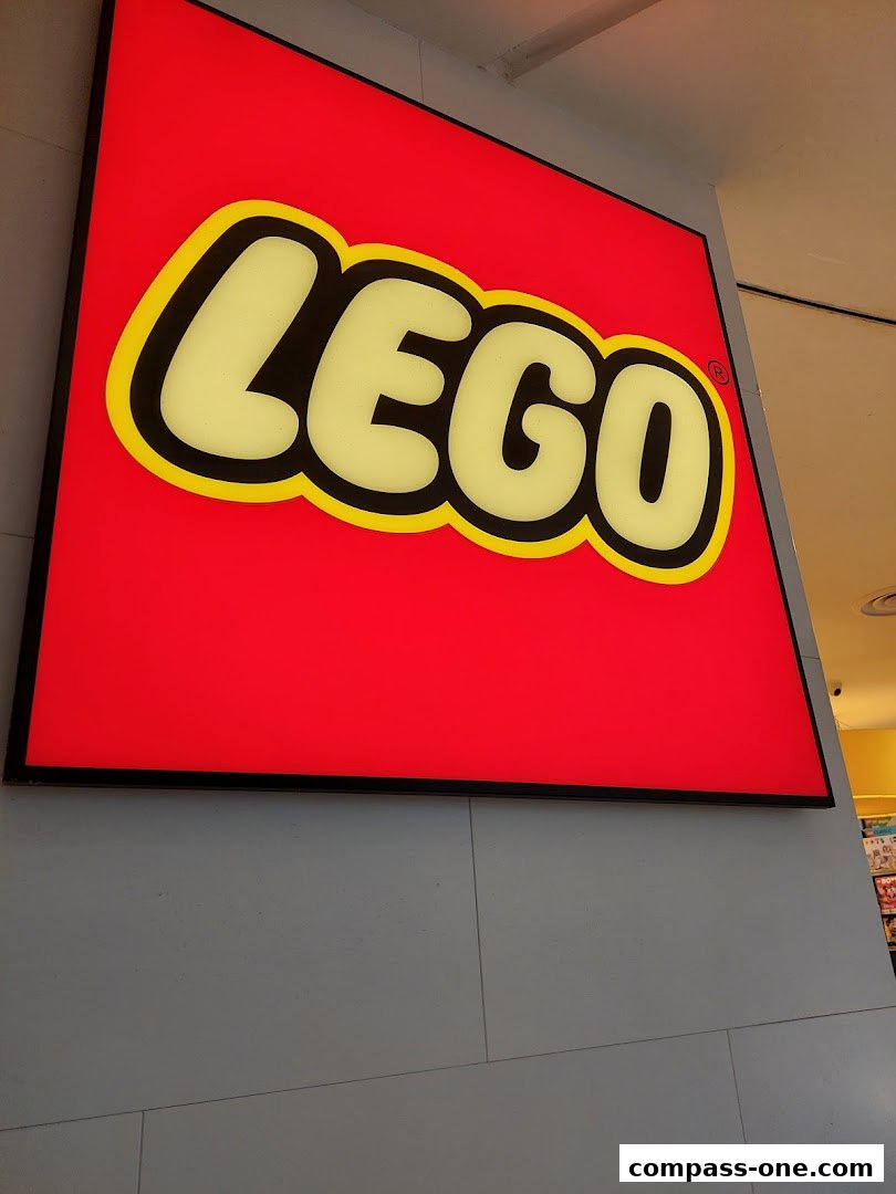 A close-up of a brightly lit LEGO logo sign on a grey tiled wall.