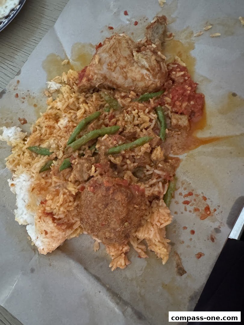 A plate of rice with chicken, vegetables, and a meatball, served on paper.