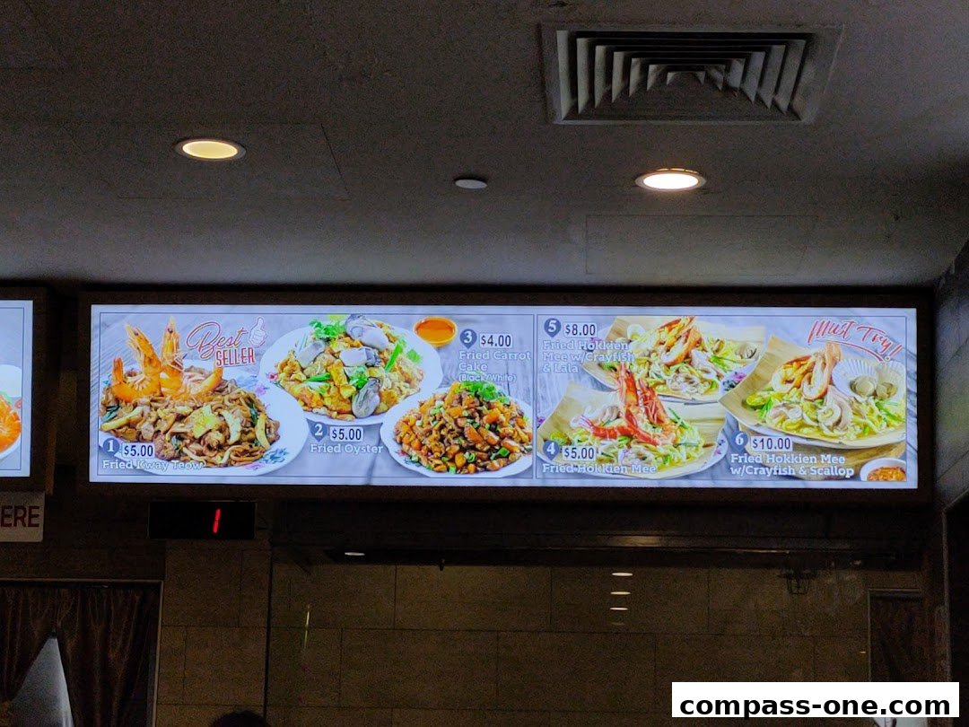 A brightly lit menu board displaying various noodle and seafood dishes with prices.