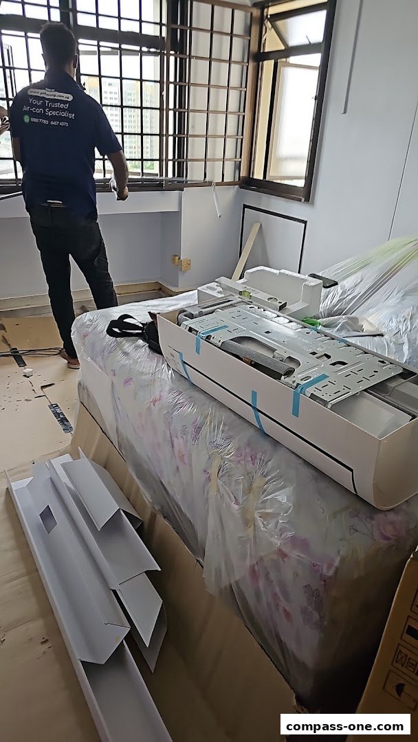 Technician installing an air conditioning unit in a room with a bed covered in plastic.