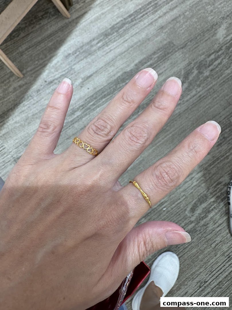 A close-up of a hand wearing two delicate gold rings, one with a heart pattern.
