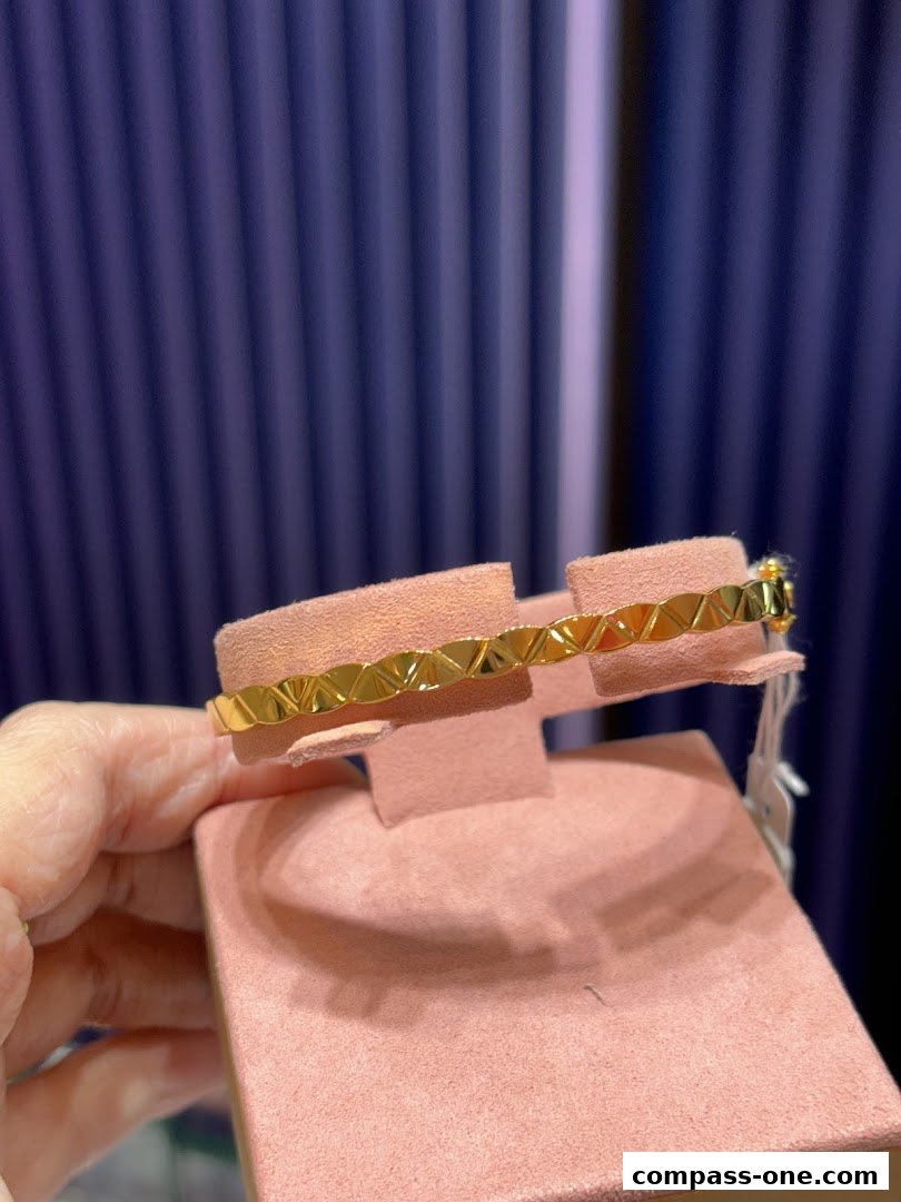 A gold bracelet with a geometric pattern displayed on a pink stand.