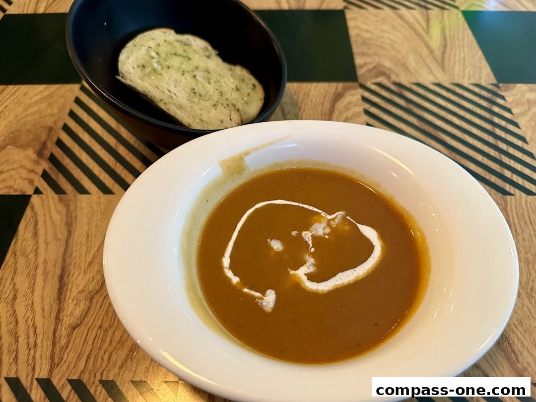 A bowl of creamy soup with a swirl of cream and a slice of garlic bread.