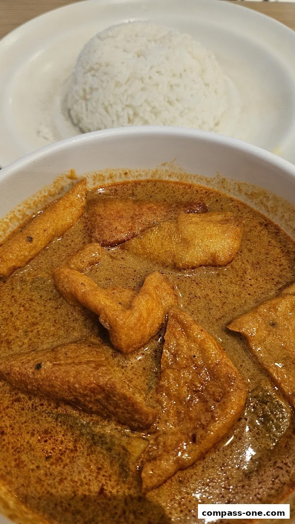 A close-up of a bowl of curry with fried fish cakes and a side of white rice.