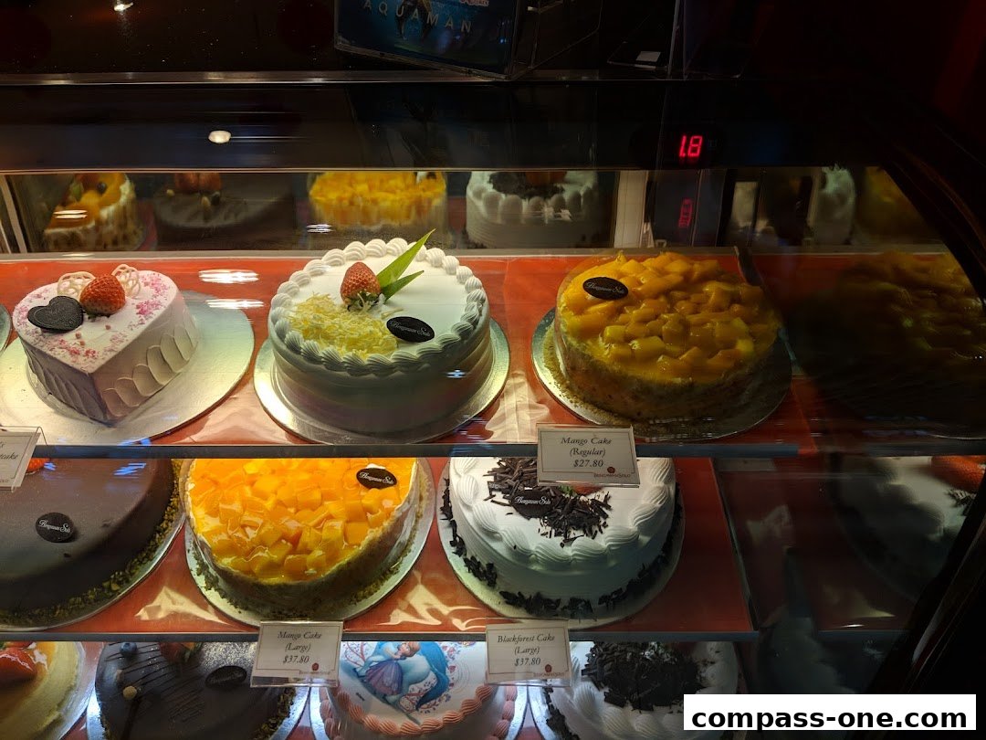 A display case filled with various beautifully decorated cakes, including heart-shaped and fruit-topped varieties.