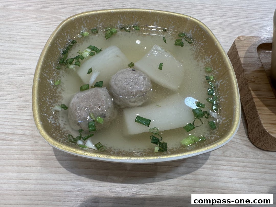 A close-up of a bowl of soup with meatballs and daikon radish, garnished with chopped scallions.