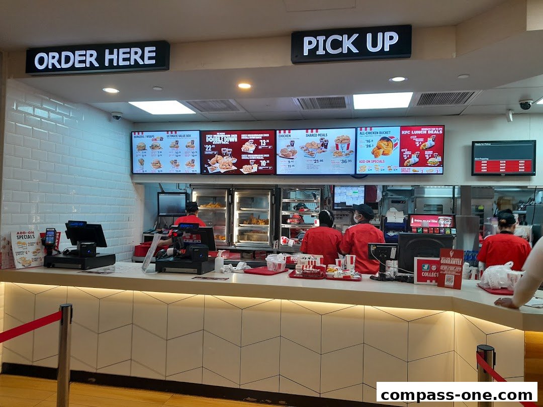 KFC counter with digital menus displaying food items and staff serving customers.