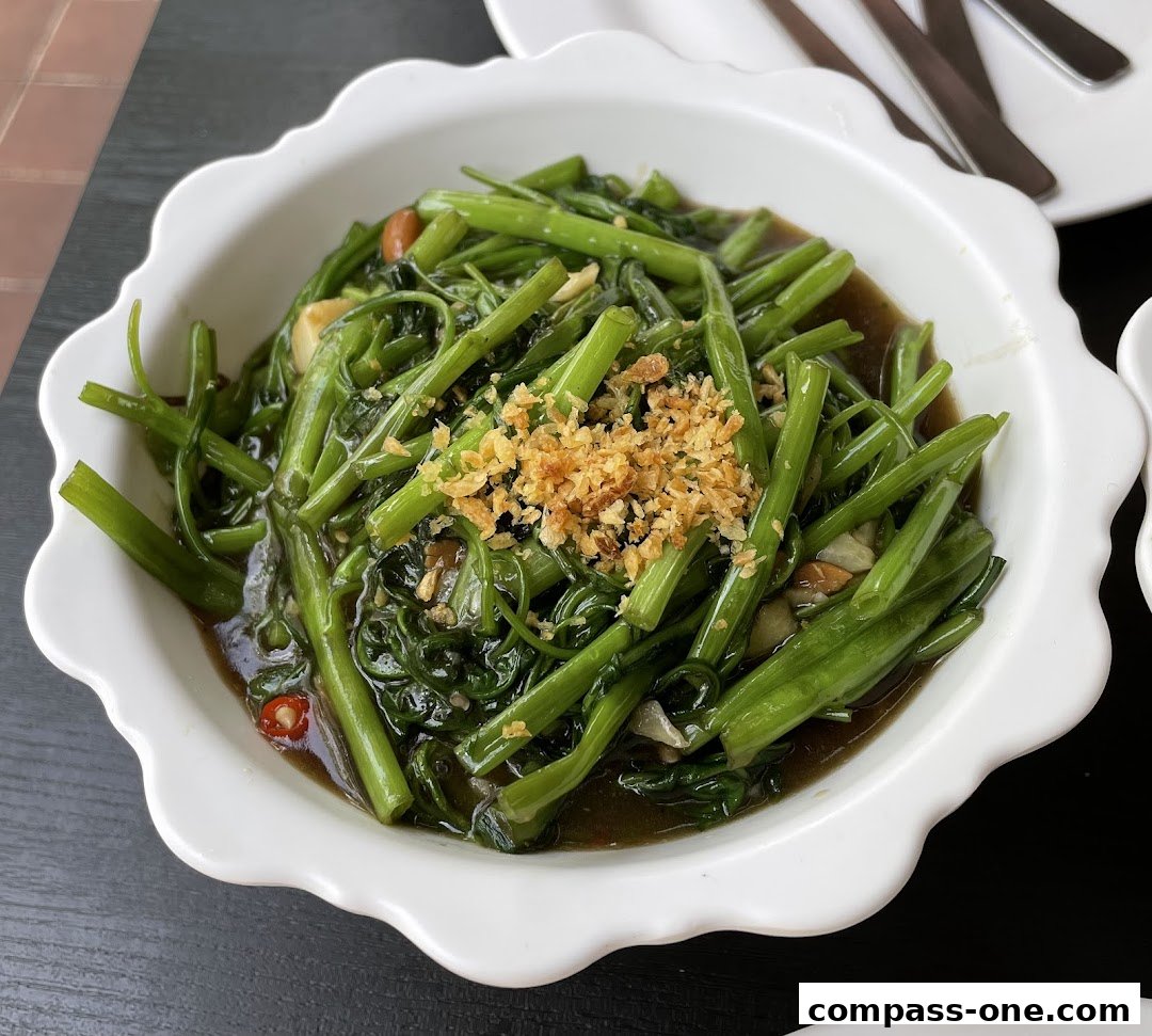 A close-up of stir-fried water spinach with garlic and chili in a white bowl.