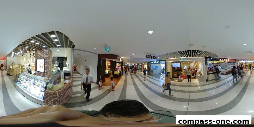 A panoramic view of a shopping mall interior with various shops and people.