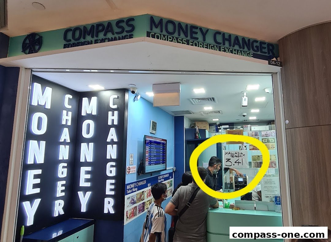 Compass Money Changer shop front with illuminated signage and currency exchange rates displayed.