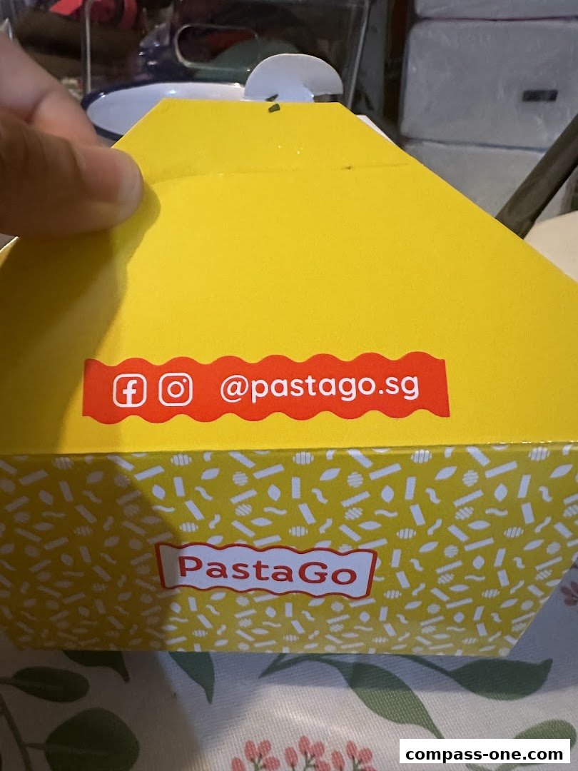 A yellow takeout box from PastaGo with social media handles and the brand logo.