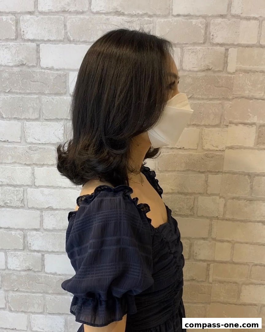 A woman with dark hair styled in soft waves, wearing a dark dress and a face mask.
