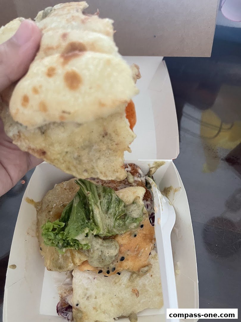 A person is holding a partially eaten burger over a takeout box with a fork.