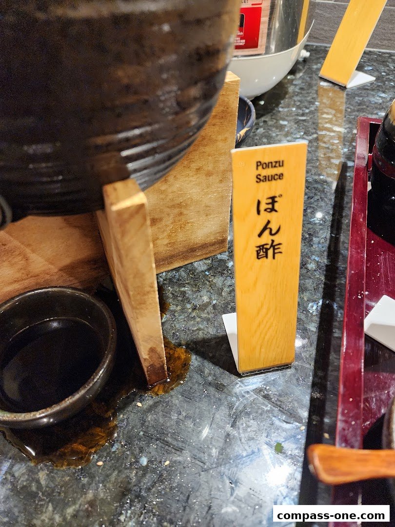 A close-up of a Ponzu sauce dispenser with a small bowl and spilled sauce.