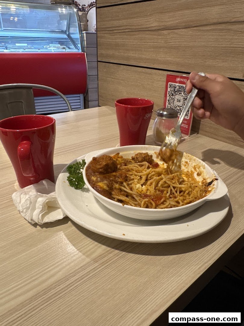 A person is eating a pasta dish at Swensens with red cups and a QR code on the table.