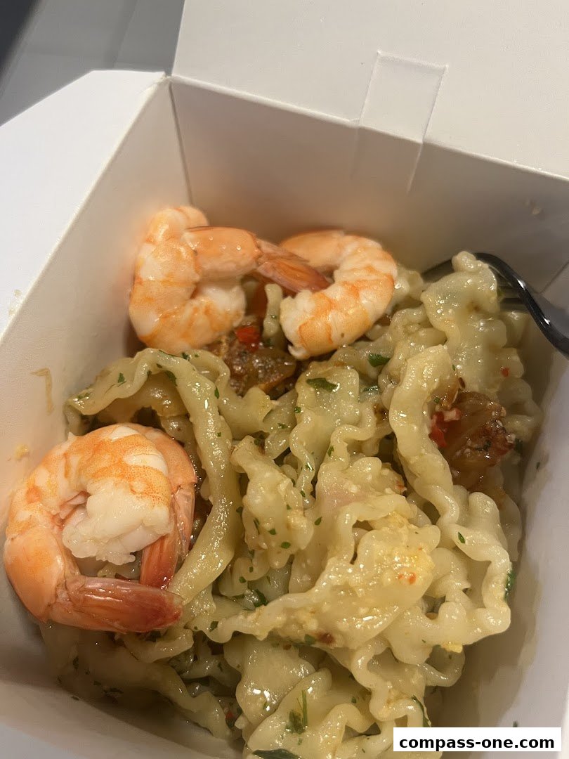 A close-up of a takeaway box filled with pasta and shrimp, ready to eat.