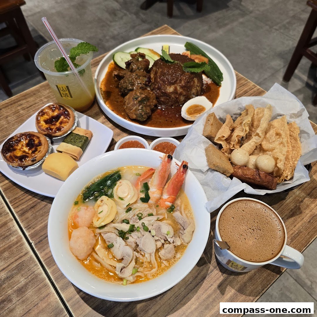 A table laden with various Ipoh delicacies including noodles, rice, pastries, and drinks.
