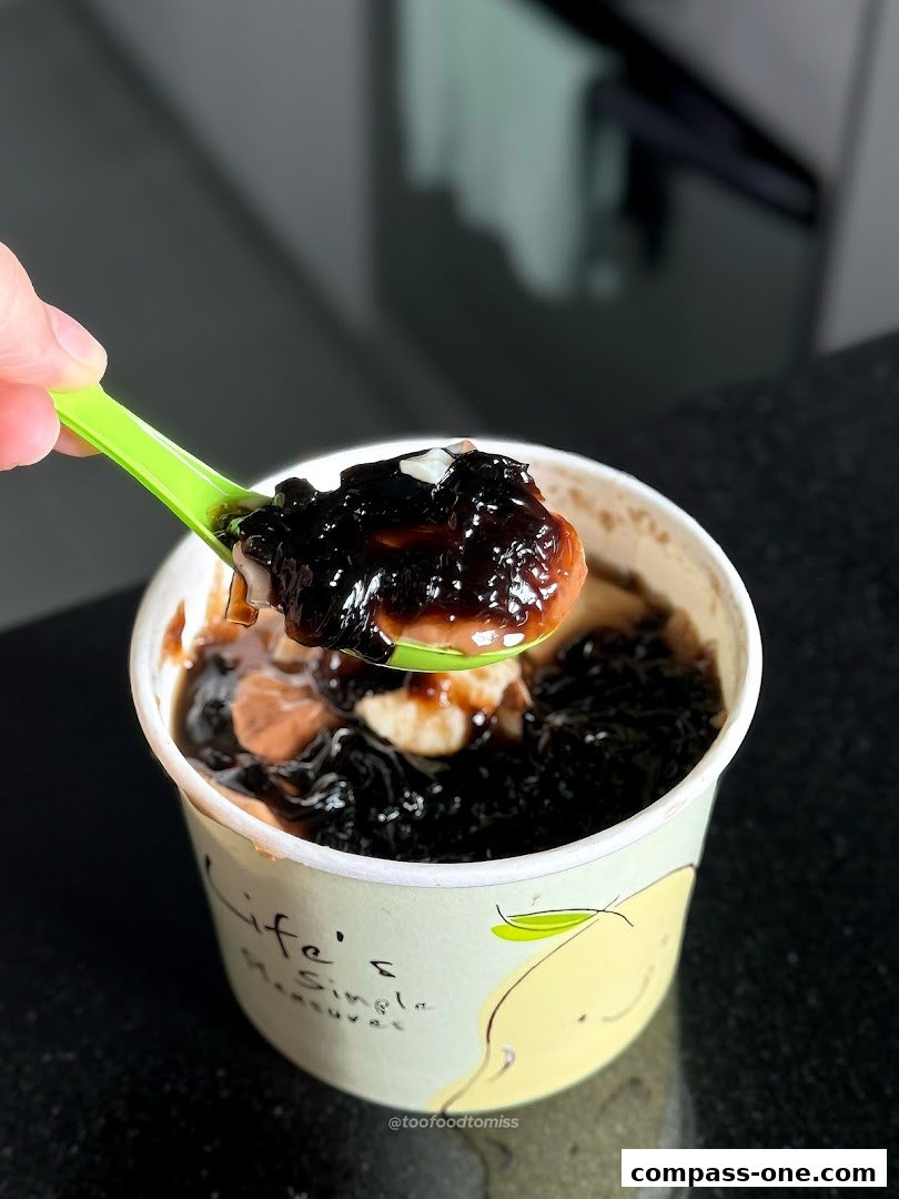A spoonful of dessert with tapioca pearls and jelly is lifted from a cup.