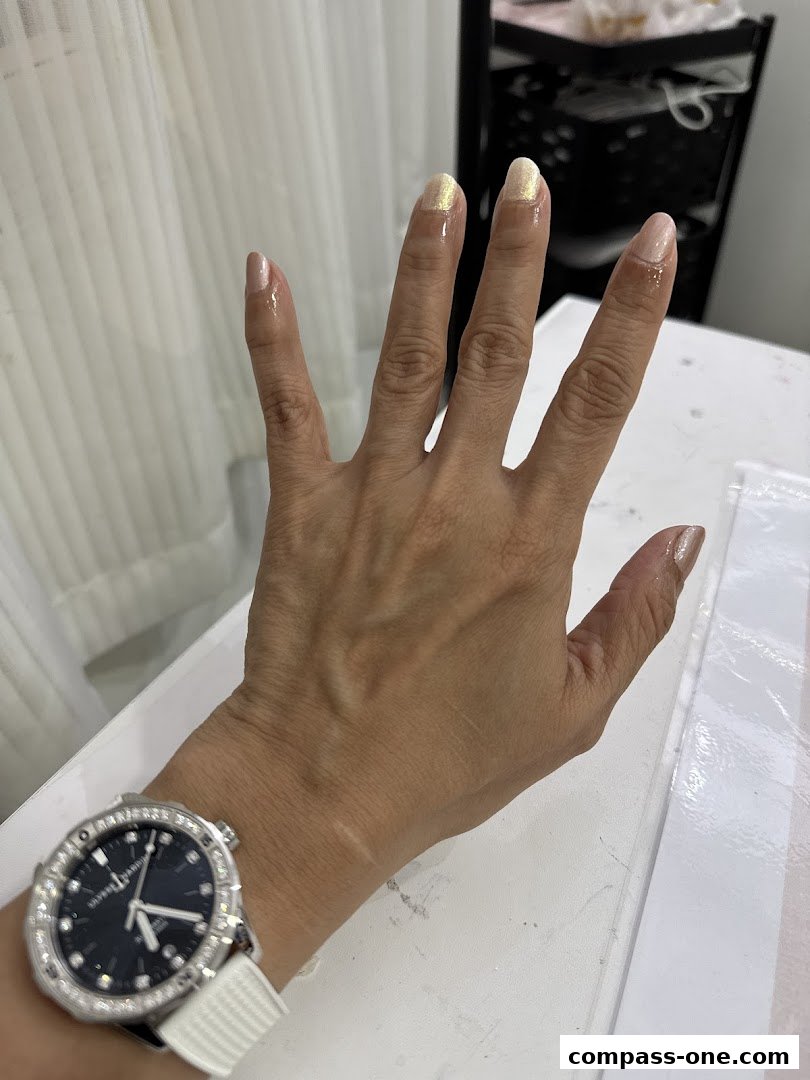 A hand with freshly painted nails, showcasing a light pink and gold shimmer polish.