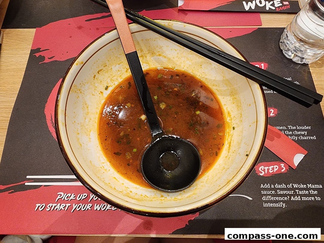 A close-up of a nearly empty ramen bowl with chopsticks and a ladle on a placemat.