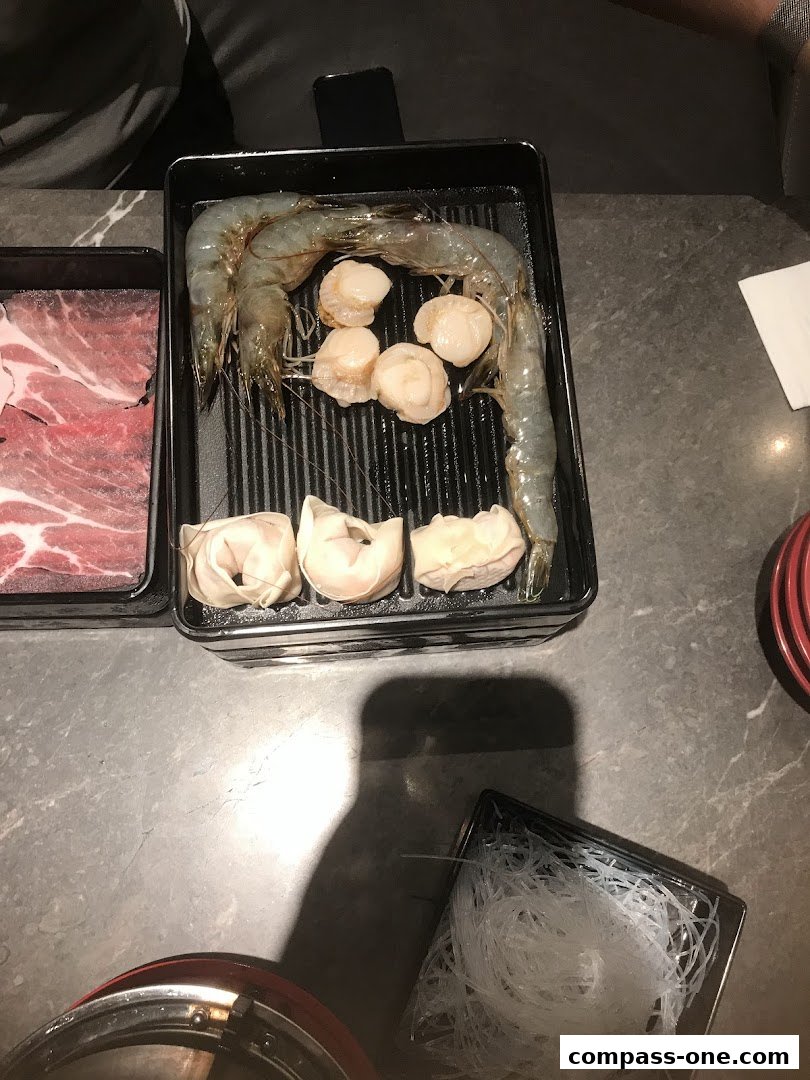 A close-up of a table with raw ingredients for hot pot, including shrimp, scallops, and meat.