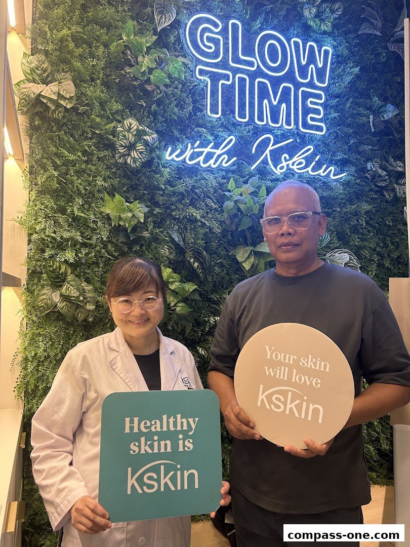 Two people stand in front of a green wall with a neon sign that says 'Glow Time with Kskin'.