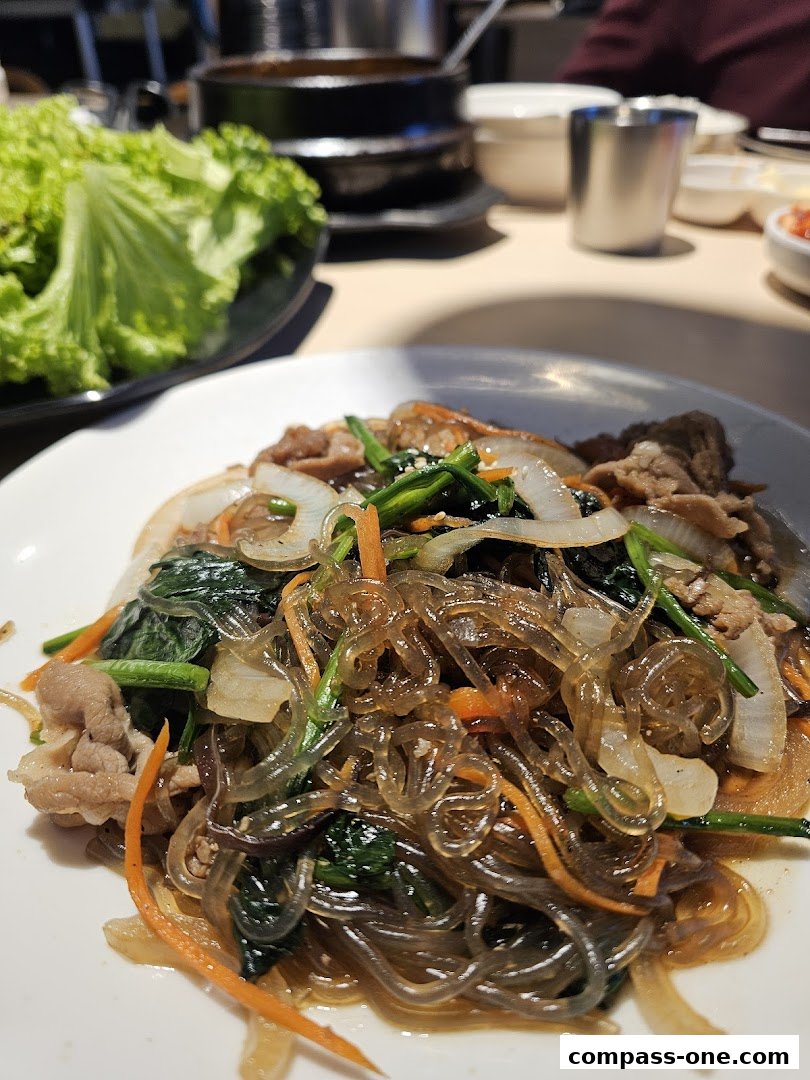 A plate of Korean Japchae with fresh lettuce and side dishes on a table.