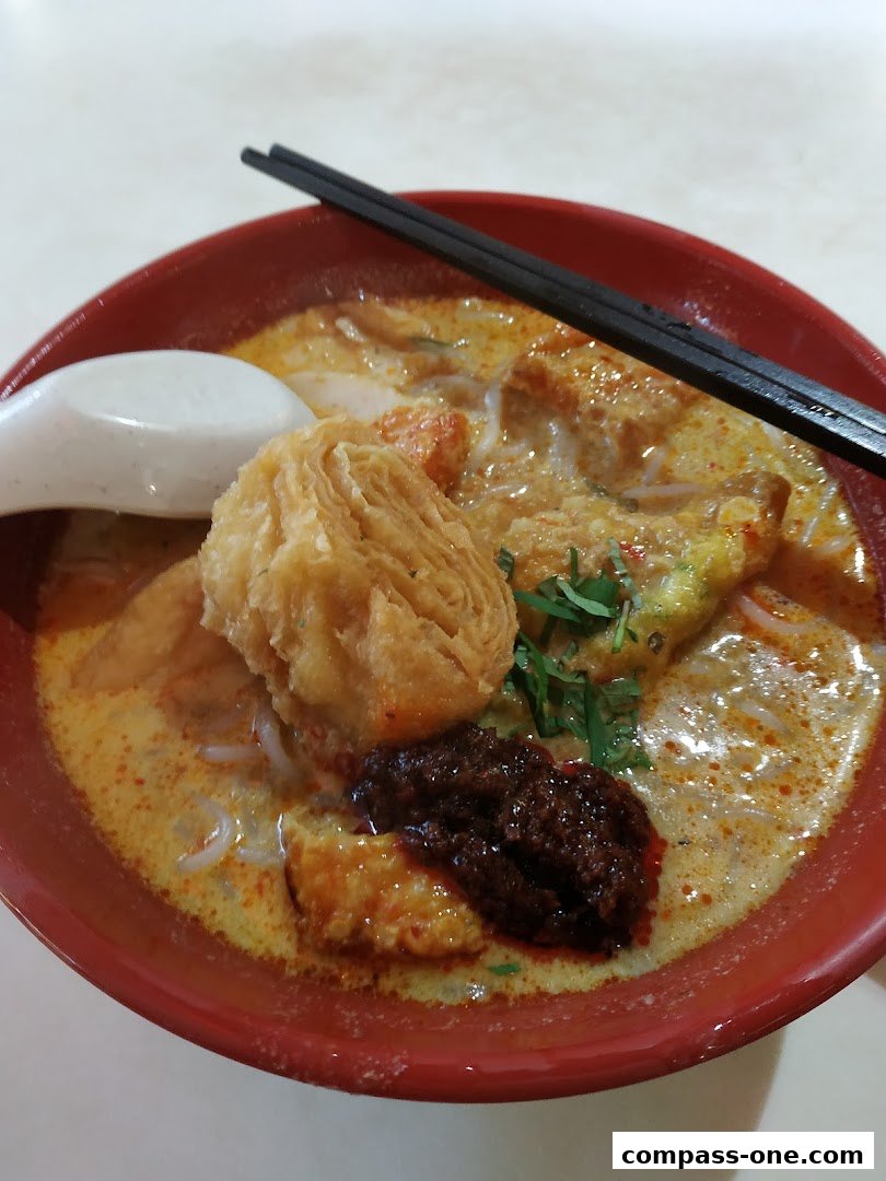 A close-up shot of a delicious bowl of curry laksa with a spoon and chopsticks.
