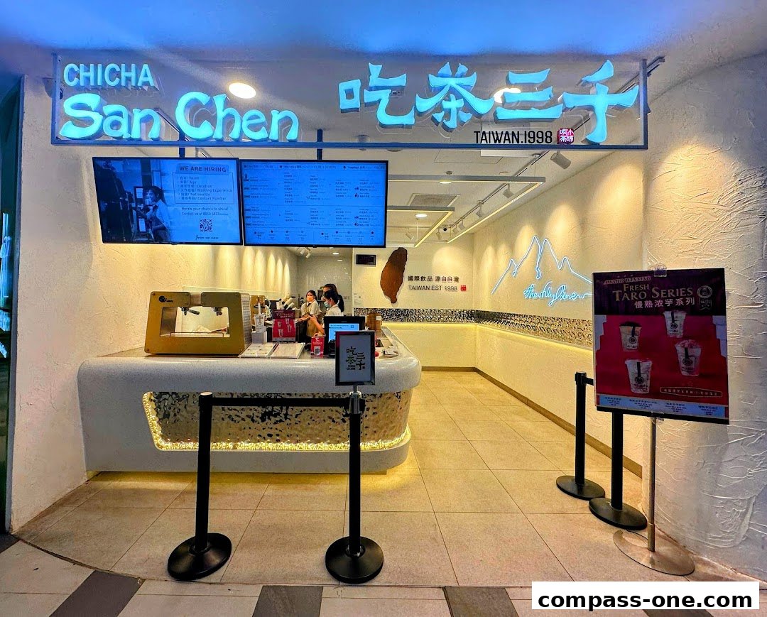 The entrance of CHICHA San Chen, a bubble tea shop, with a bright neon sign and menu displays.