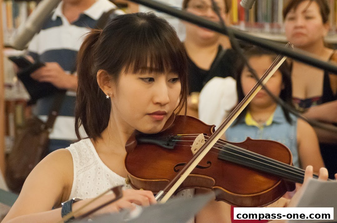 A young woman plays the violin in front of an audience at a music school.