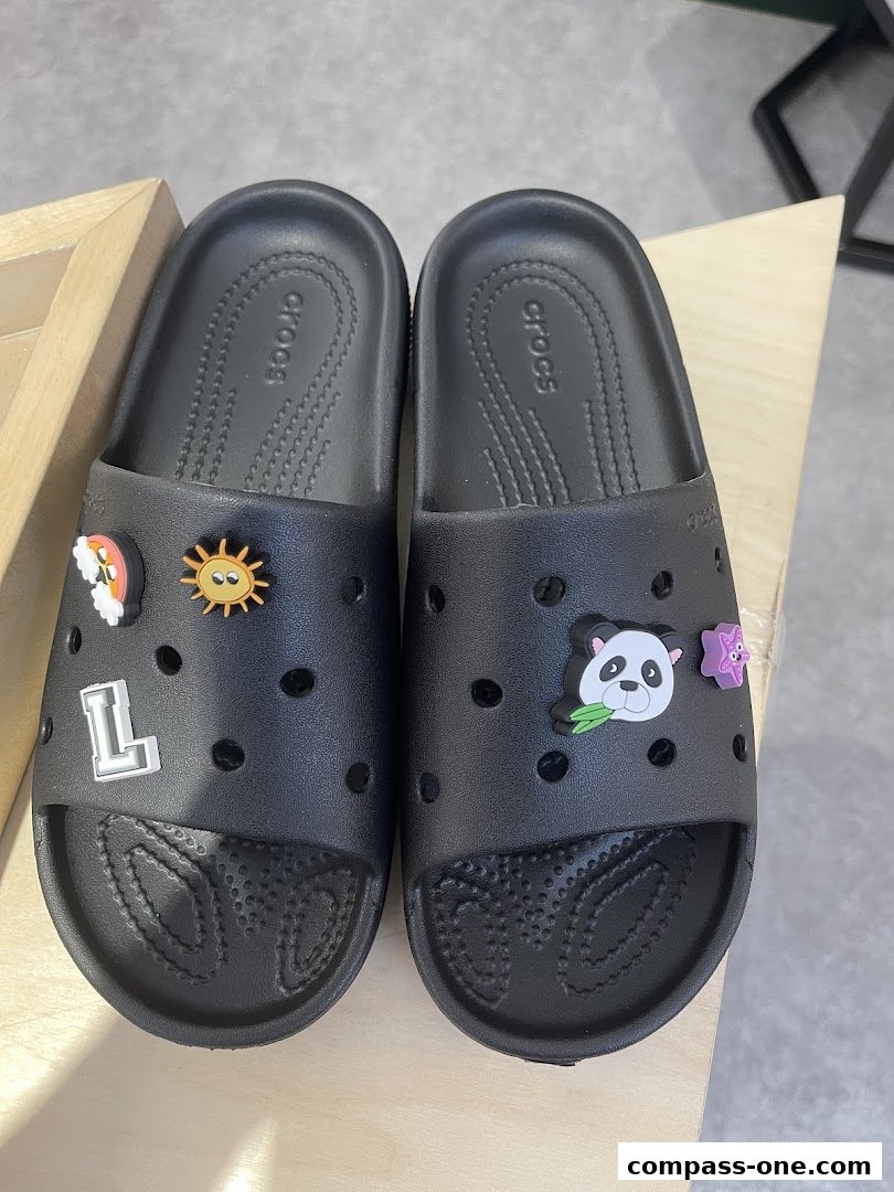 Black Crocs slides decorated with fun Jibbitz charms like a panda and a rainbow.