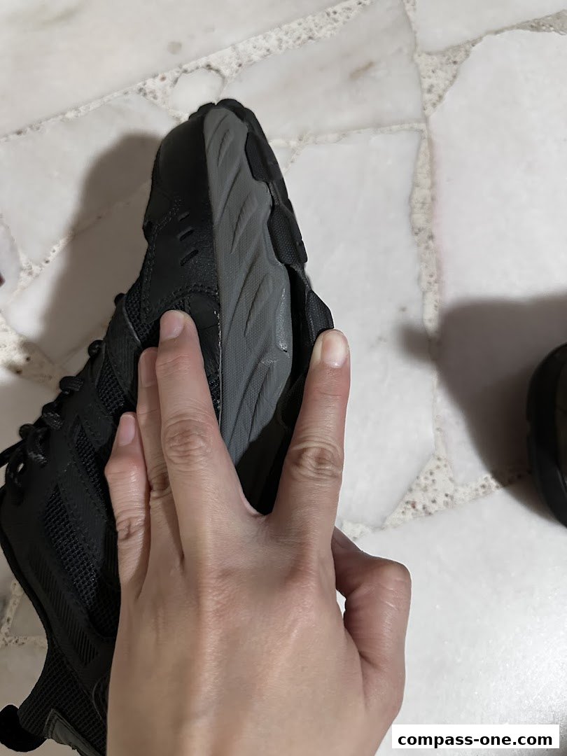 A hand is holding a black shoe, showing the sole and side.