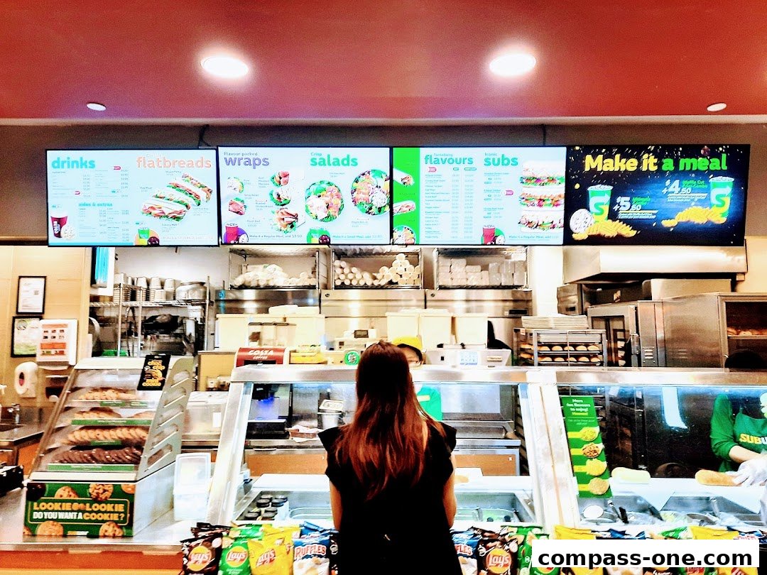 A Subway restaurant interior with digital menus displaying drinks, flatbreads, wraps, salads, flavors, and subs.