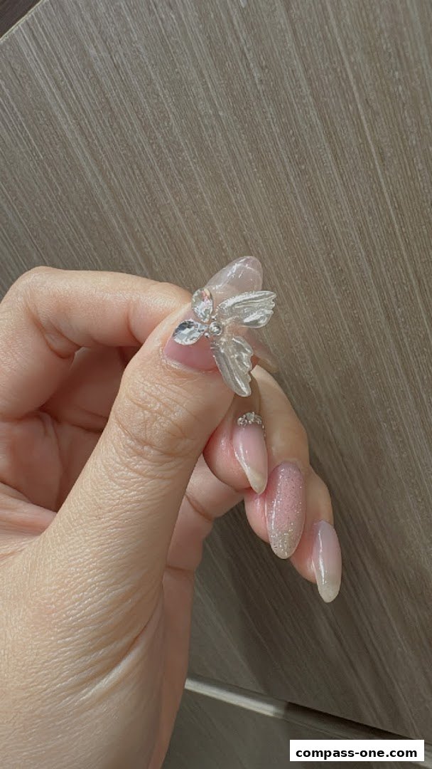 A close-up of a hand with beautifully decorated nails featuring a 3D flower embellishment and glitter.