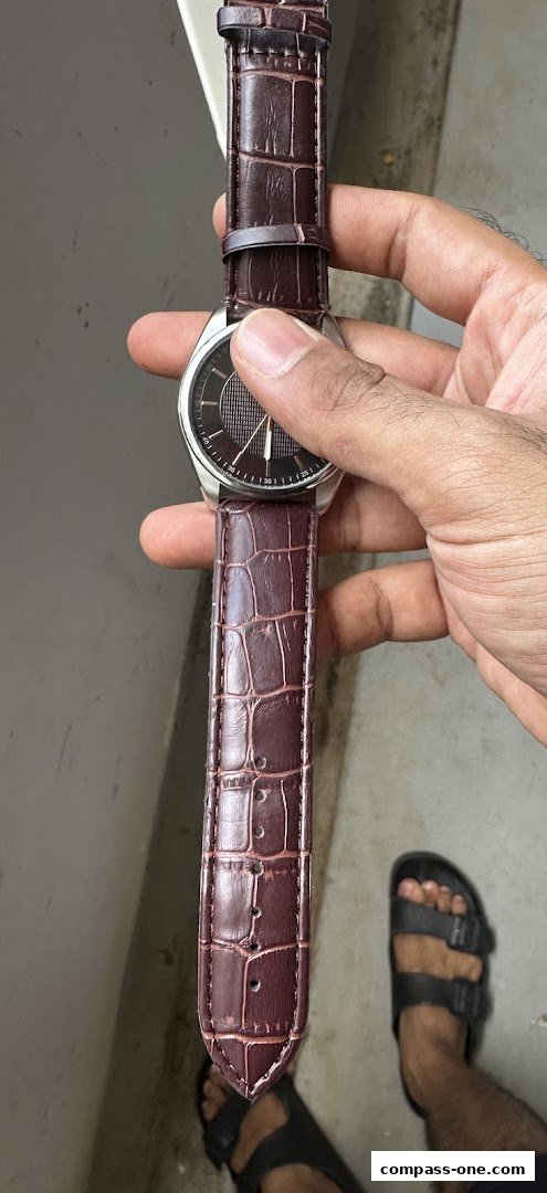 A person holds a stylish watch with a dark brown crocodile-patterned leather strap.