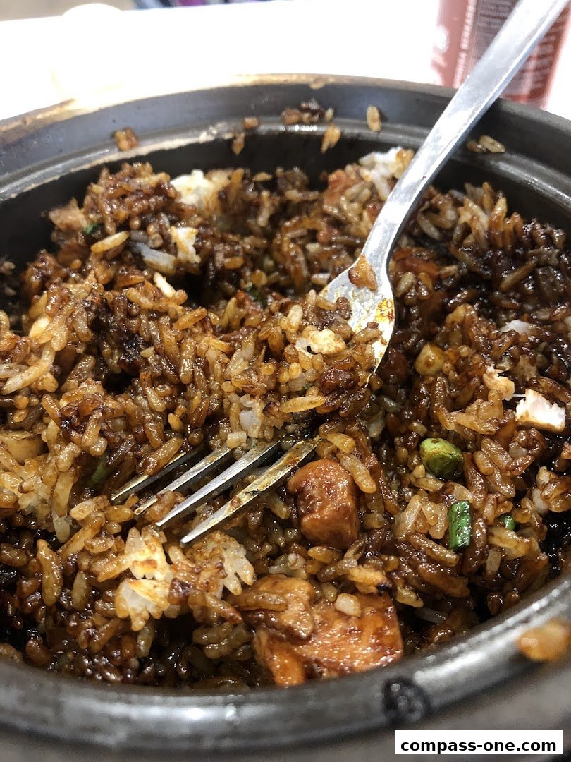 A close-up shot of a fork digging into a bowl of savory fried rice with chicken.