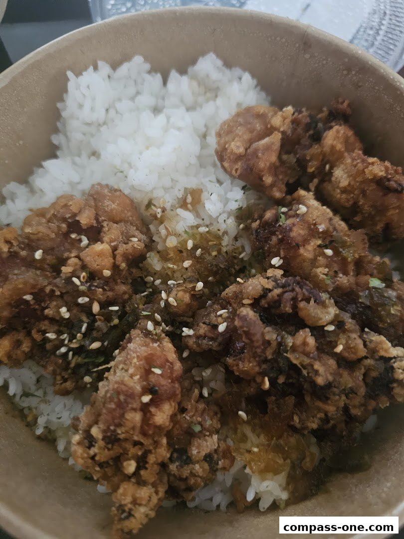 A close-up of a bowl of rice topped with crispy fried chicken pieces and sesame seeds.