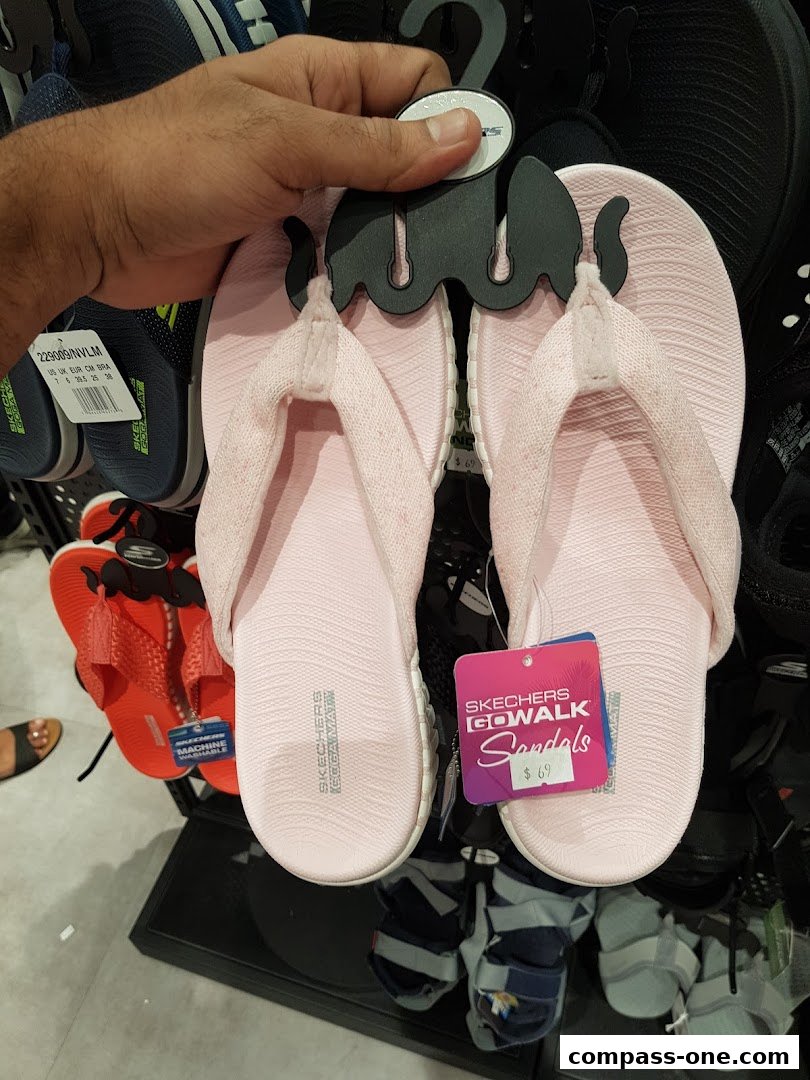 A hand holds a pair of pink Skechers Go Walk sandals with price tags.