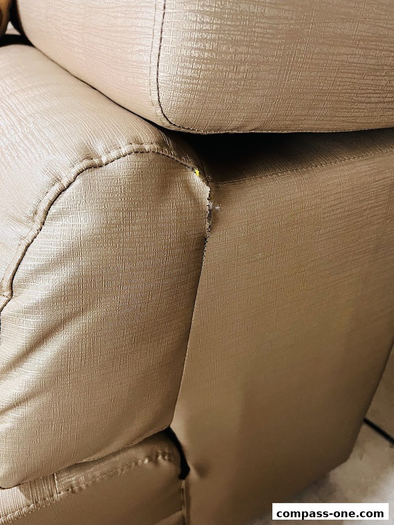 Close-up of a beige leather sofa with visible stitching and a small tear.
