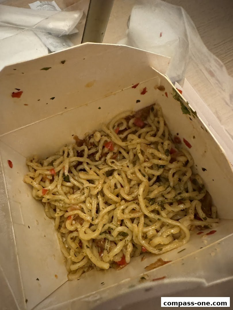 A close-up shot of freshly made pasta in a takeaway box, with visible herbs and red pepper flakes.