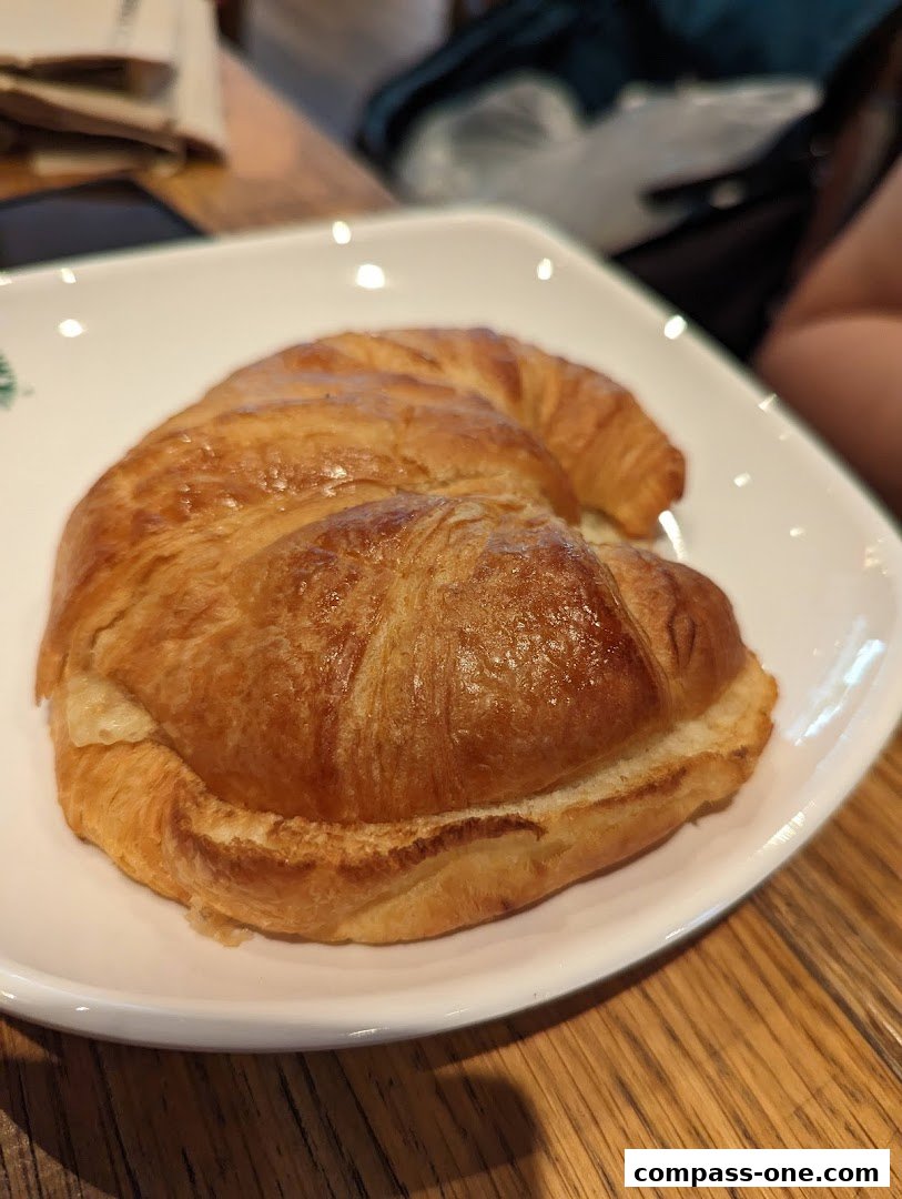 A golden-brown croissant is served on a white plate with the Starbucks logo.