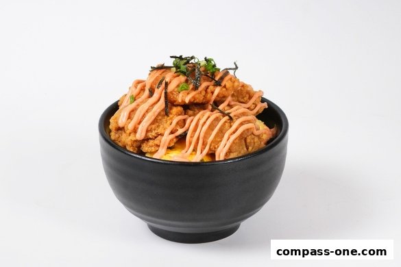 A black bowl filled with crispy fried chicken, drizzled with sauce and topped with seaweed and green onions.