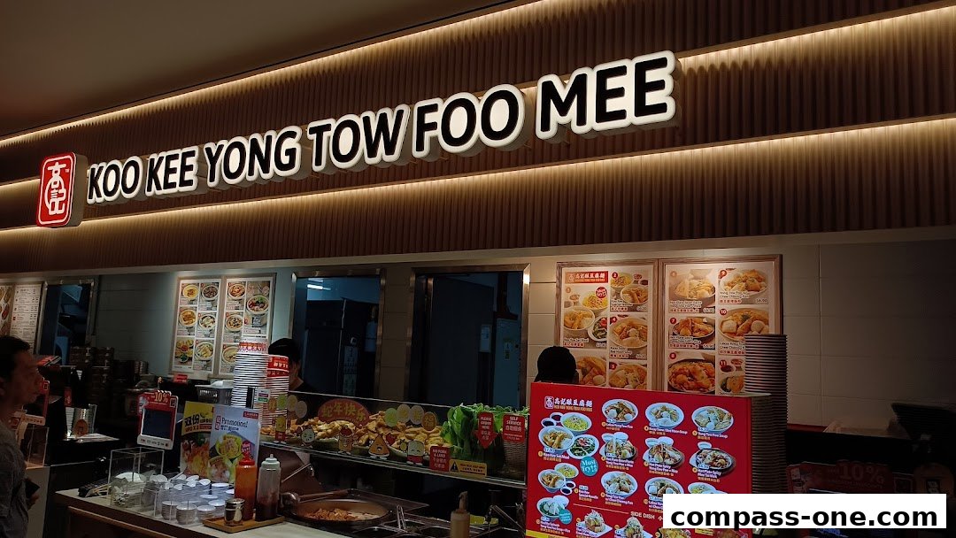 The illuminated sign for Koo Kee Yong Tow Foo Mee above a food stall with menu displays.